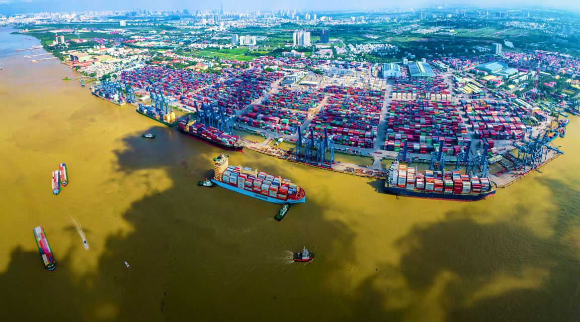 A massive port system with huge quantities of colorful shipping containers and large cargo ships on a greenish waterway