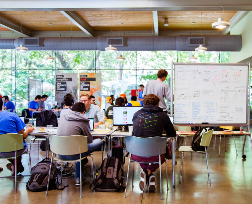 A small gathering of young professionals in a modern classroom with wall-to-wall sunlit windows 