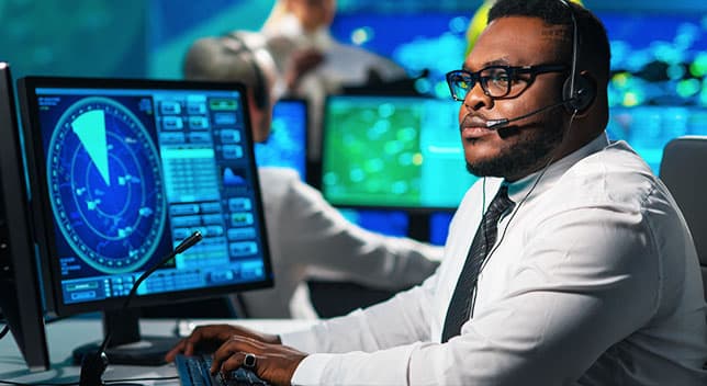Persona con auriculares sentada frente a una pantalla de ordenador en la que se muestra el tráfico aéreo en un radar