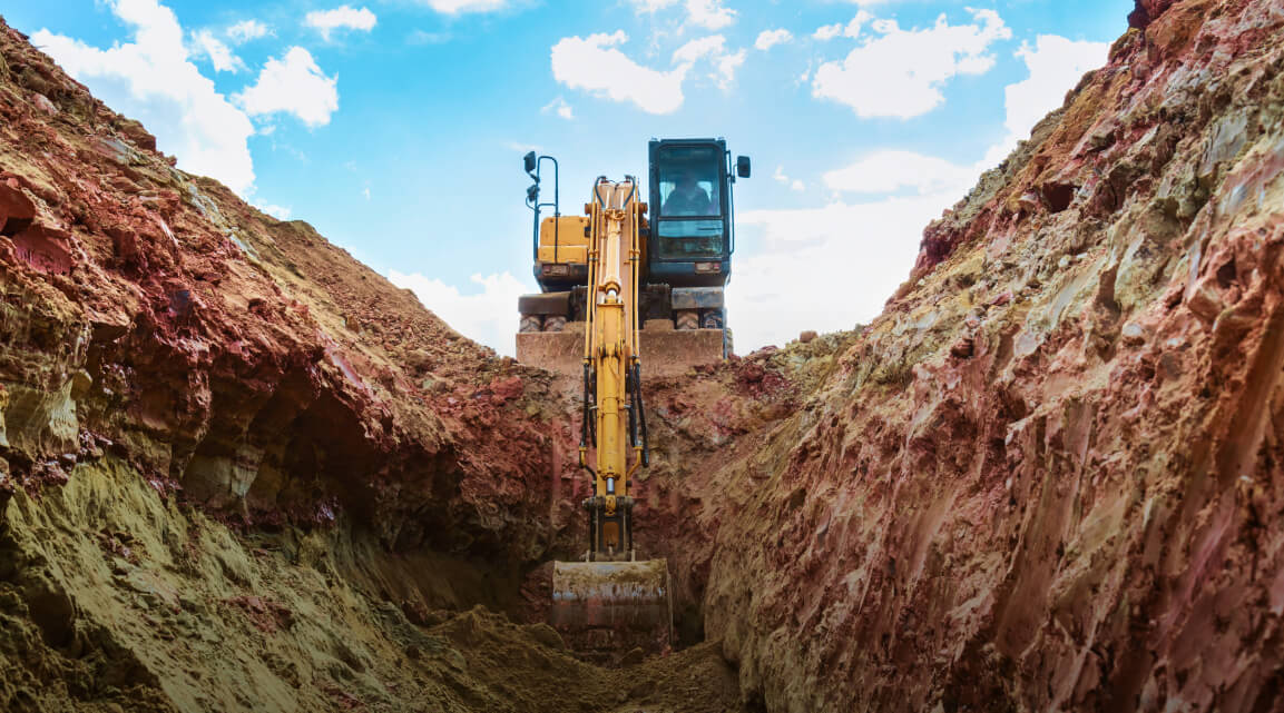 Pelleteuse creusant dans un large fossé au milieu de terre rocailleuse rougeâtre