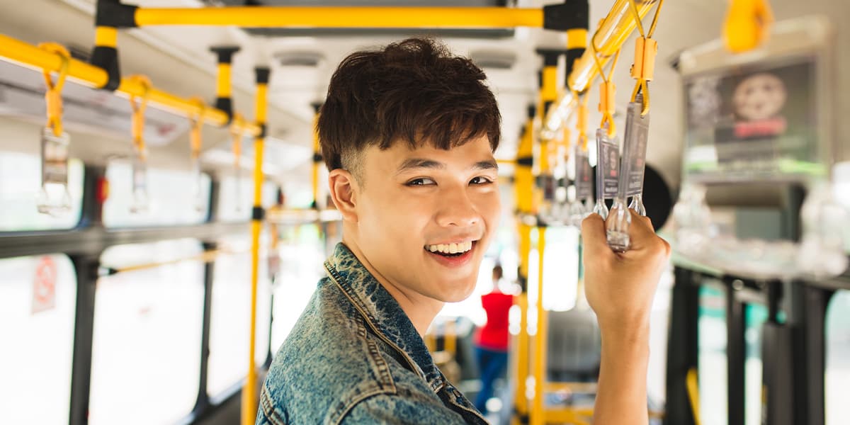 A happy young adult taking public transportation, standing on a bus