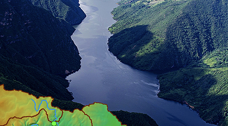 An aerial photo of a broad blue river winding through large green tree-covered mountains with a small colorful map in the corner