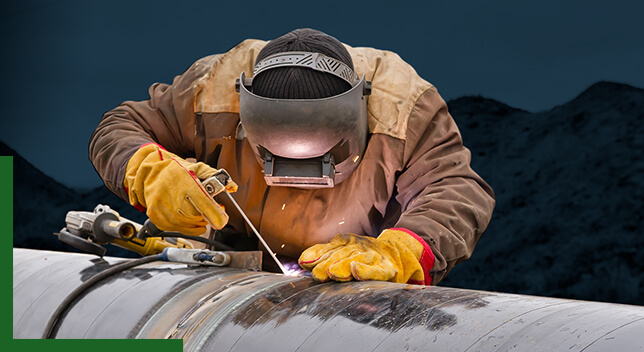 A person in protective gear welding a pipeline