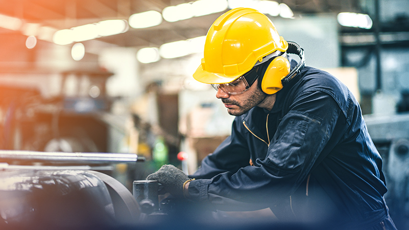 Persona con casco amarillo y gafas de seguridad utilizando una pieza de maquinaria pesada en un taller industrial