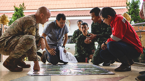 A team of people kneeling, attentively studying a map on the floor of the Thai cave where 13 people were trapped and needed rescuing.