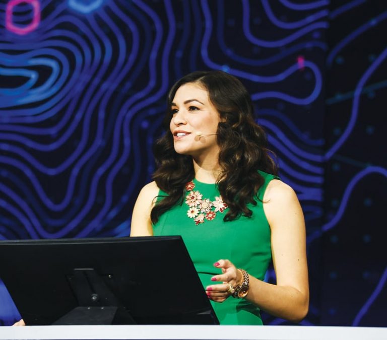 A photo of Jennifer Bell talking into a microphone, giving a presentation onstage