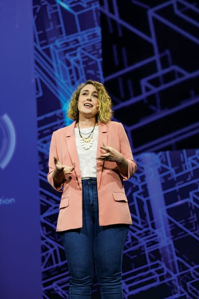 A photo of Lauren Bennett speaking into a microphone while giving a presentation onstage