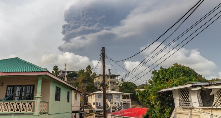 Colorful houses with a plume of volcanic ash rising behind them