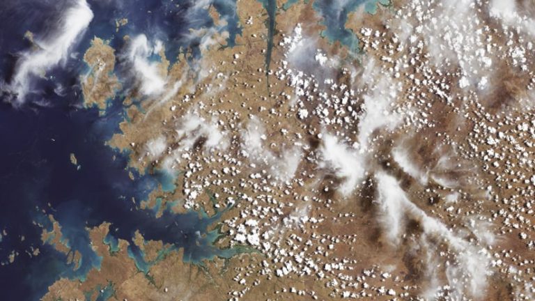 Landsat aerial imagery that shows the ocean with islands and a lot of brown land dotted with small clouds