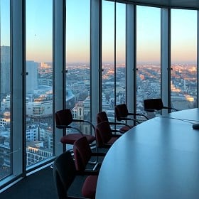 a round conference table with floor-to-ceiling windows behind it