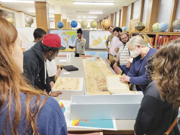 About 11 people stand around a table covered with maps.