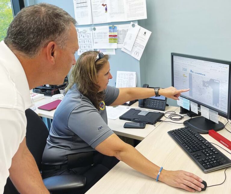 An individual points to a computer screen while another individual looks on.