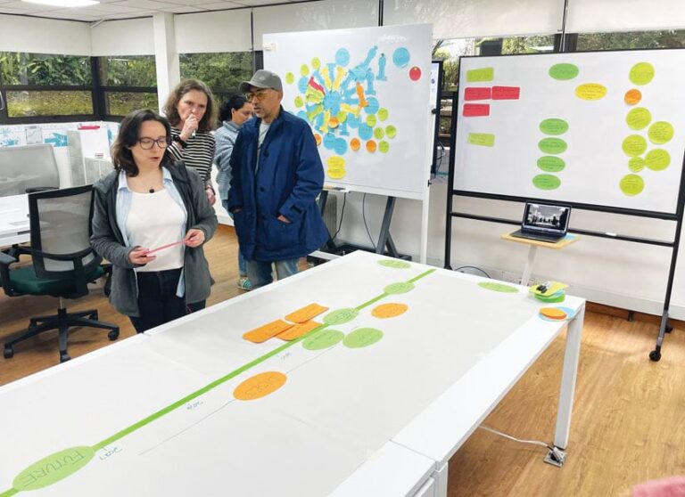 Four people stand in a room with three whiteboards.