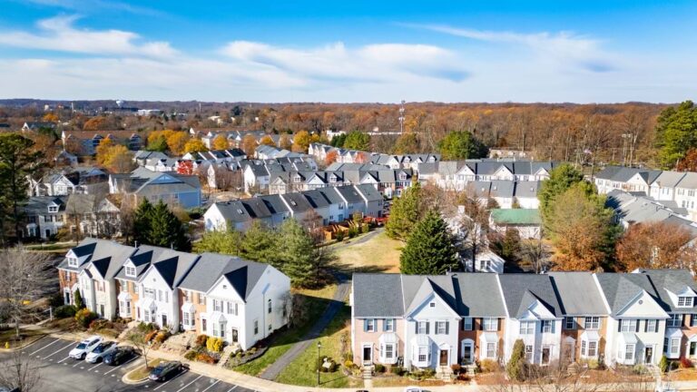 Aerial view of a dense suburban neighborhood with rows of townhomes and single-family homes surrounded by fall foliage.