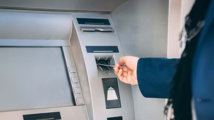 A hand holds a card near an ATM.