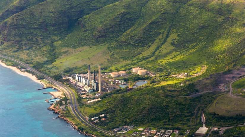 A factory sits on the edge of a lush coastal area