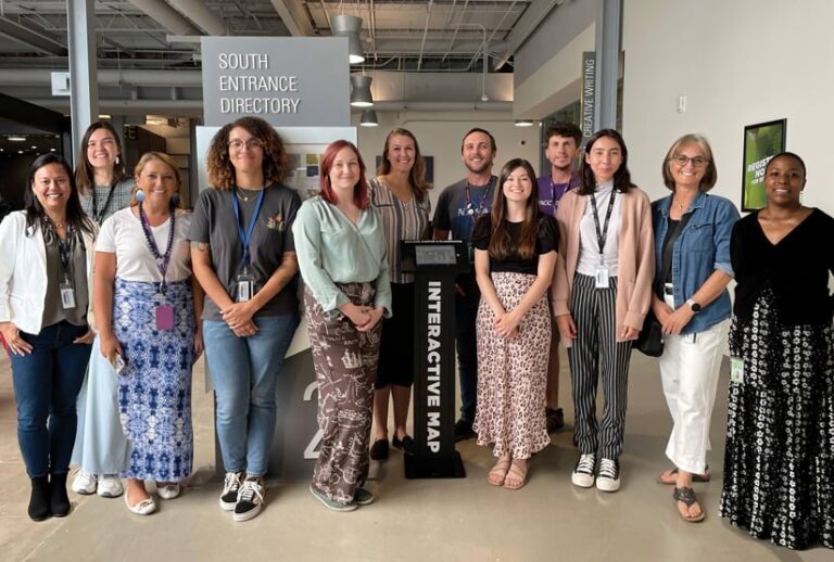 A group of people posing for a photo beside a kiosk labelled “Interactive Map.”