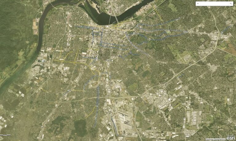 Aerial view of Louisville, Kentucky, showing the city's layout, roads, and airport. Blue and yellow lines overlay some roads, indicating roadways that have been improved and those marked for reconfiguration, respectively.