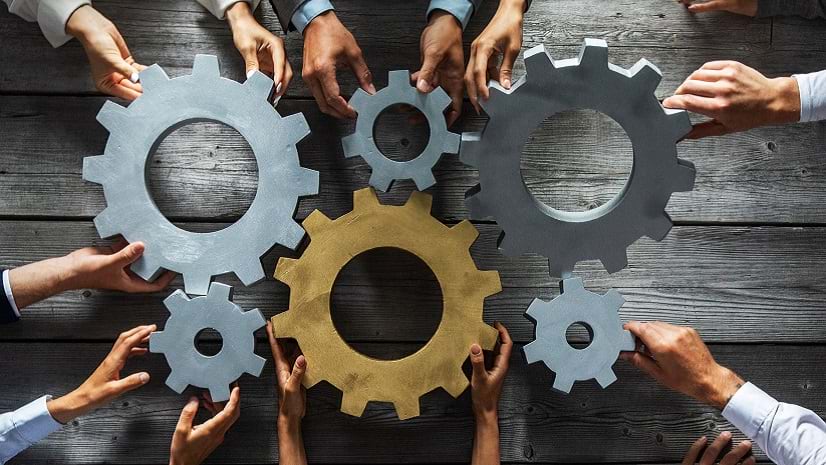 A group of people joining together silver and golden colored gears on a table