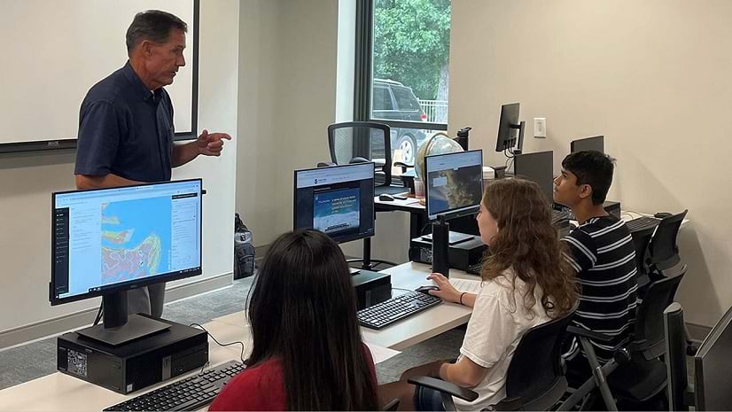 A teacher instructs three students at computers