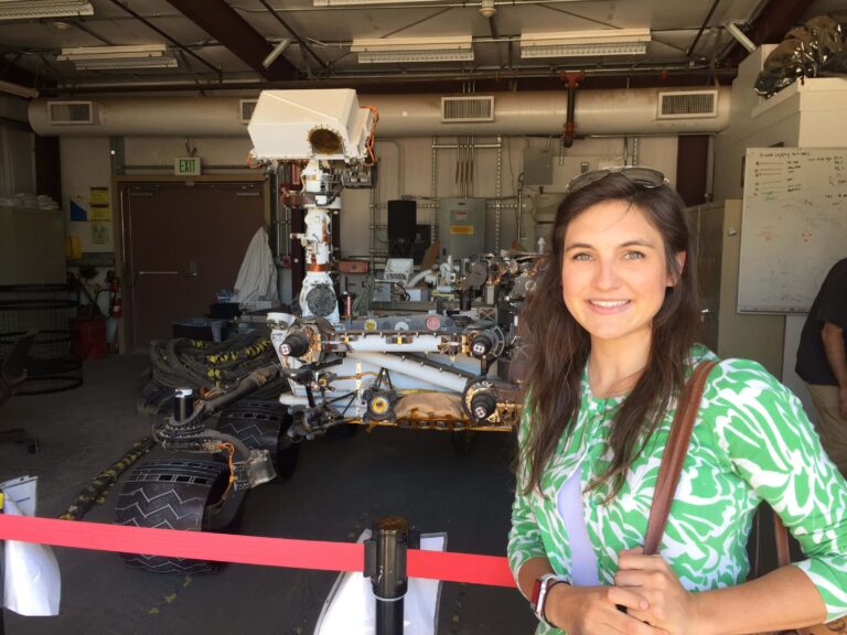 A smiling young woman standing next to machinery