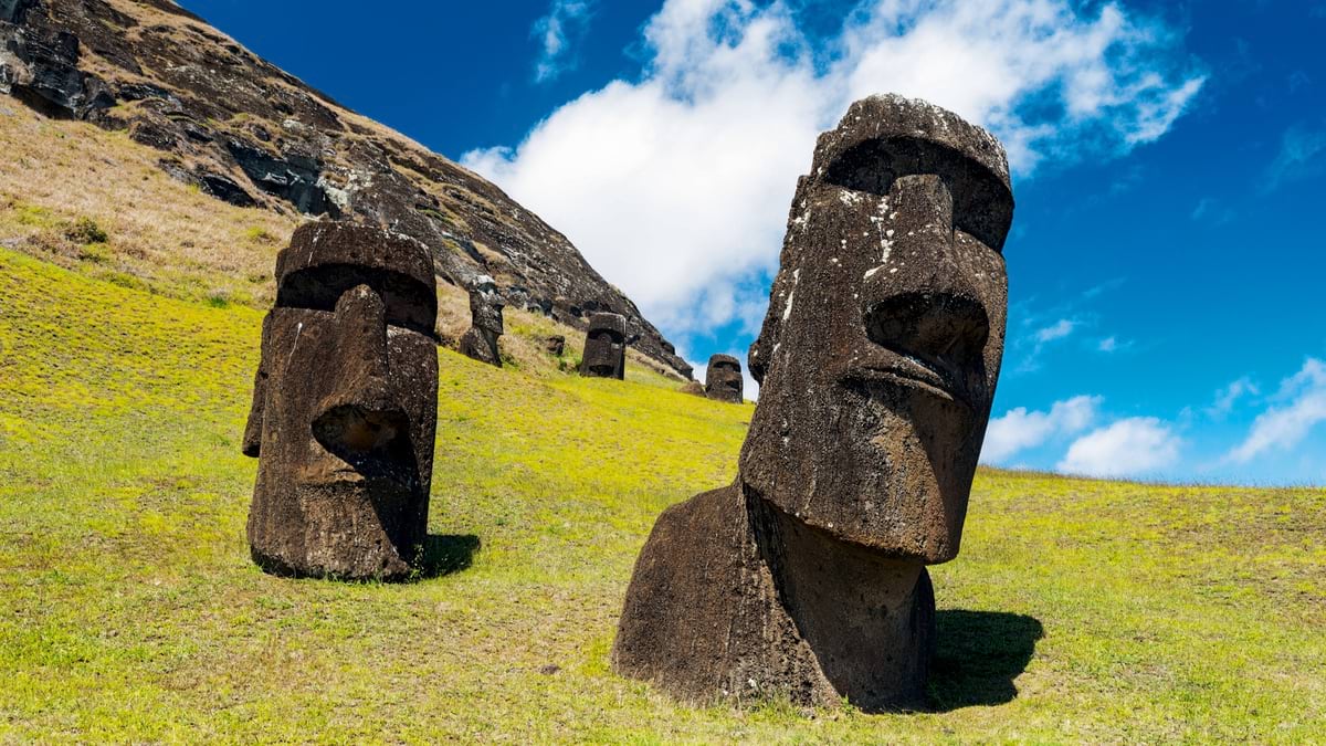 Two moai statues on grassy volcanic slope with additional statues visible on hillside behind them.