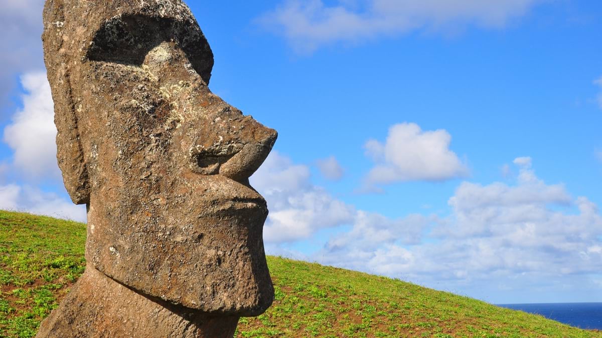Close-up profile view of weathered moai statue against blue sky and ocean background.