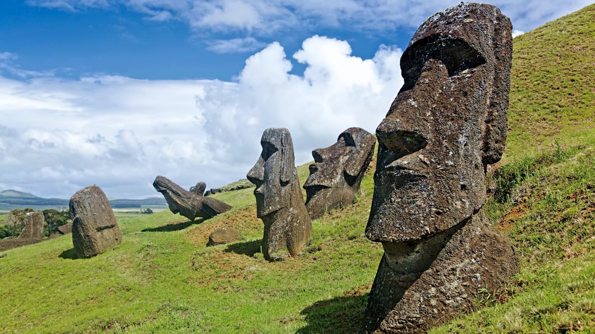Multiple moai statues on green hillside, some standing upright and others toppled or tilted.