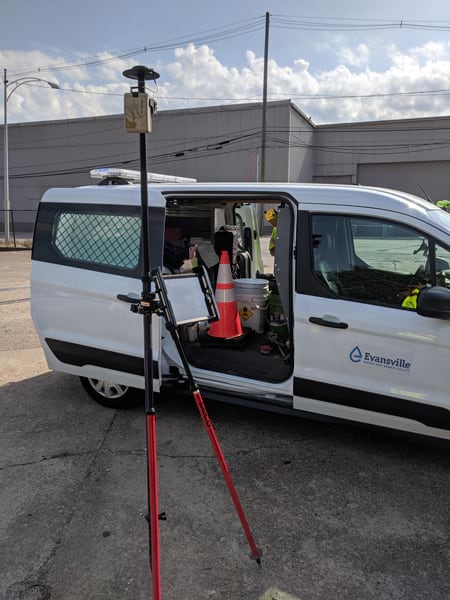 Photograph of a white van with an Evansville water logo on the door. A GNSS receiver is set up beside the van with a tablet mounted to it.