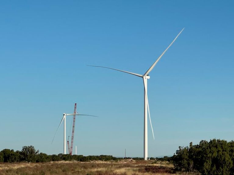 Photograph of a complete wind turbine in the foreground. In the background, another turbine is under construction, with two of three blades installed.