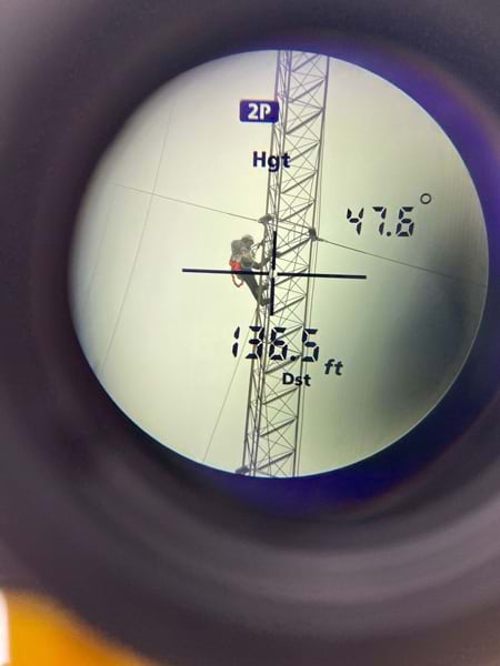 Wide shot of a man climbing a cell tower, overlaid with a rangefinder display.