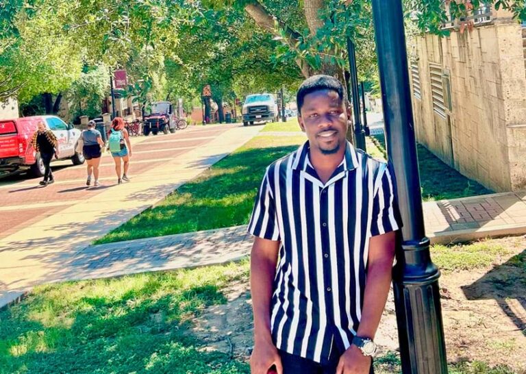 A smiling man leaning against a light pole.