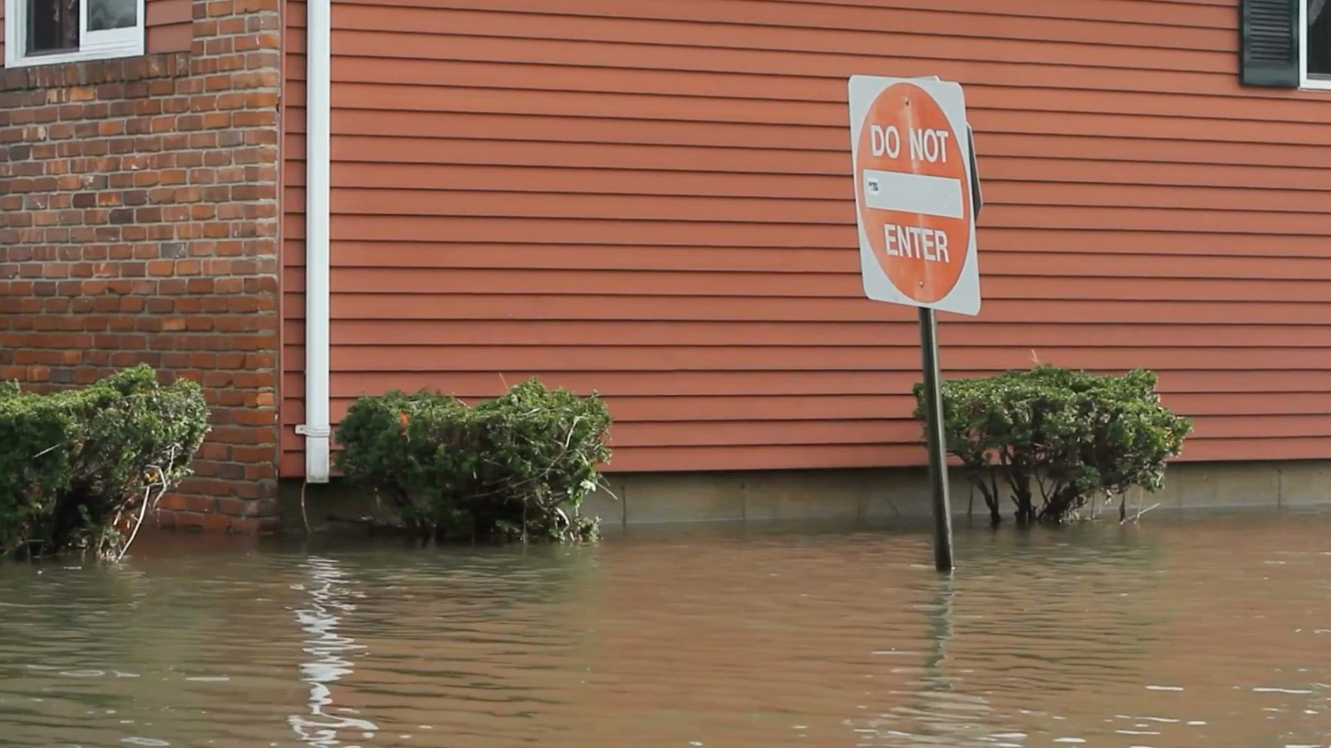 Floodwater covering the foundation of a home and the pole of a road sign