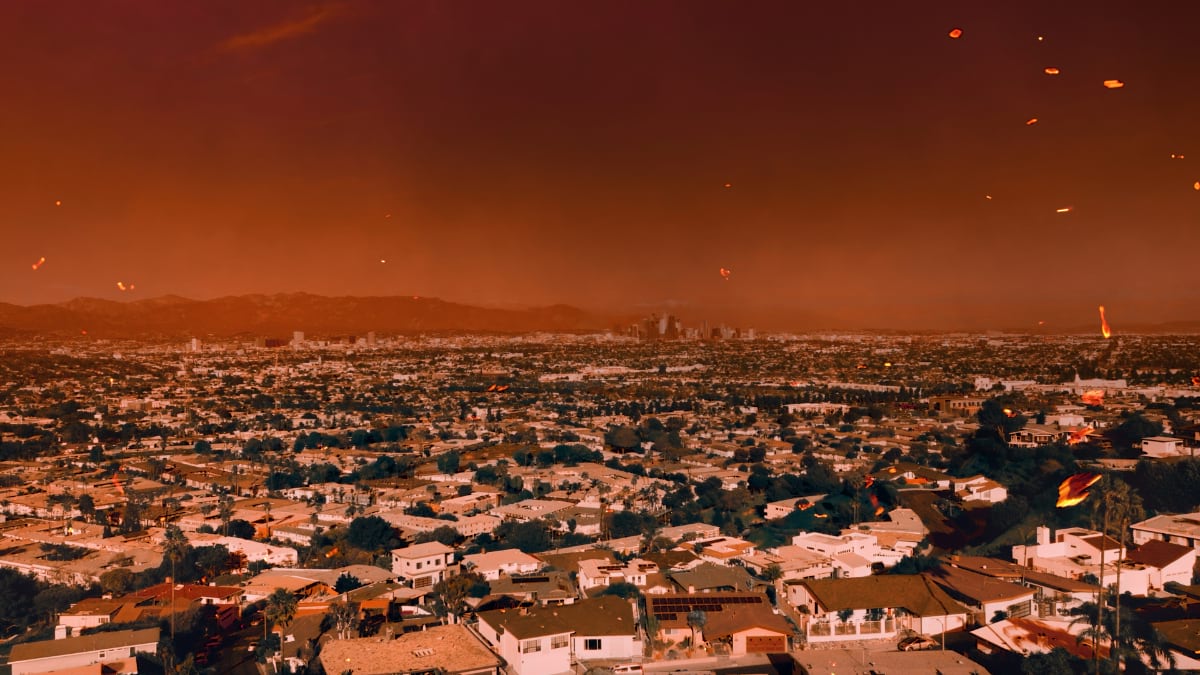 Aerial view of a Southern California residential neighborhood with orange-tinted sky filled with smoke and scattered fire embers, showing the wildfire threat to densely populated suburban communities.