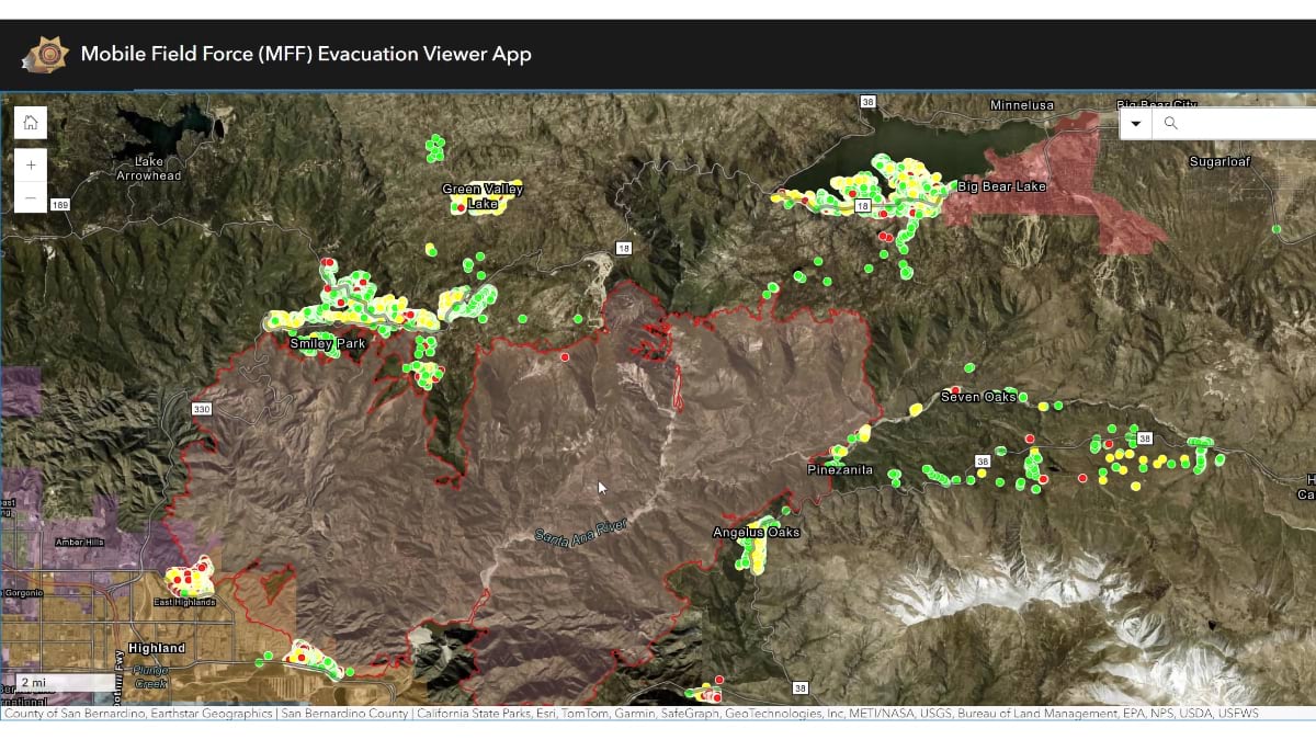 San Bernardino County's Mobile Field Force evacuation app showing a satellite map of mountainous terrain with fire perimeters outlined in red and color-coded dots (green, red, yellow) marking evacuation status of individual homes across communities like Big Bear Lake, Seven Oaks, and Pinezanita.