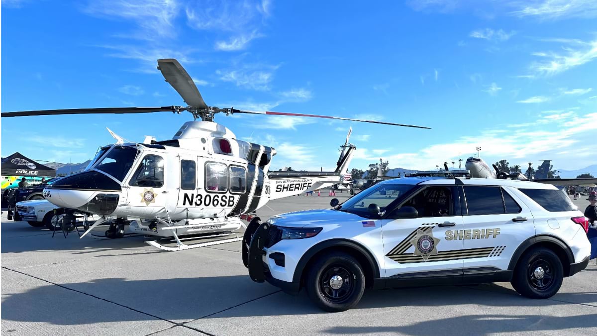San Bernardino County Sheriff helicopter and patrol vehicle on airport tarmac under blue sky, showing the multi-platform emergency response capabilities used during wildfire evacuations and emergency operations across the county's 20,000 square miles.