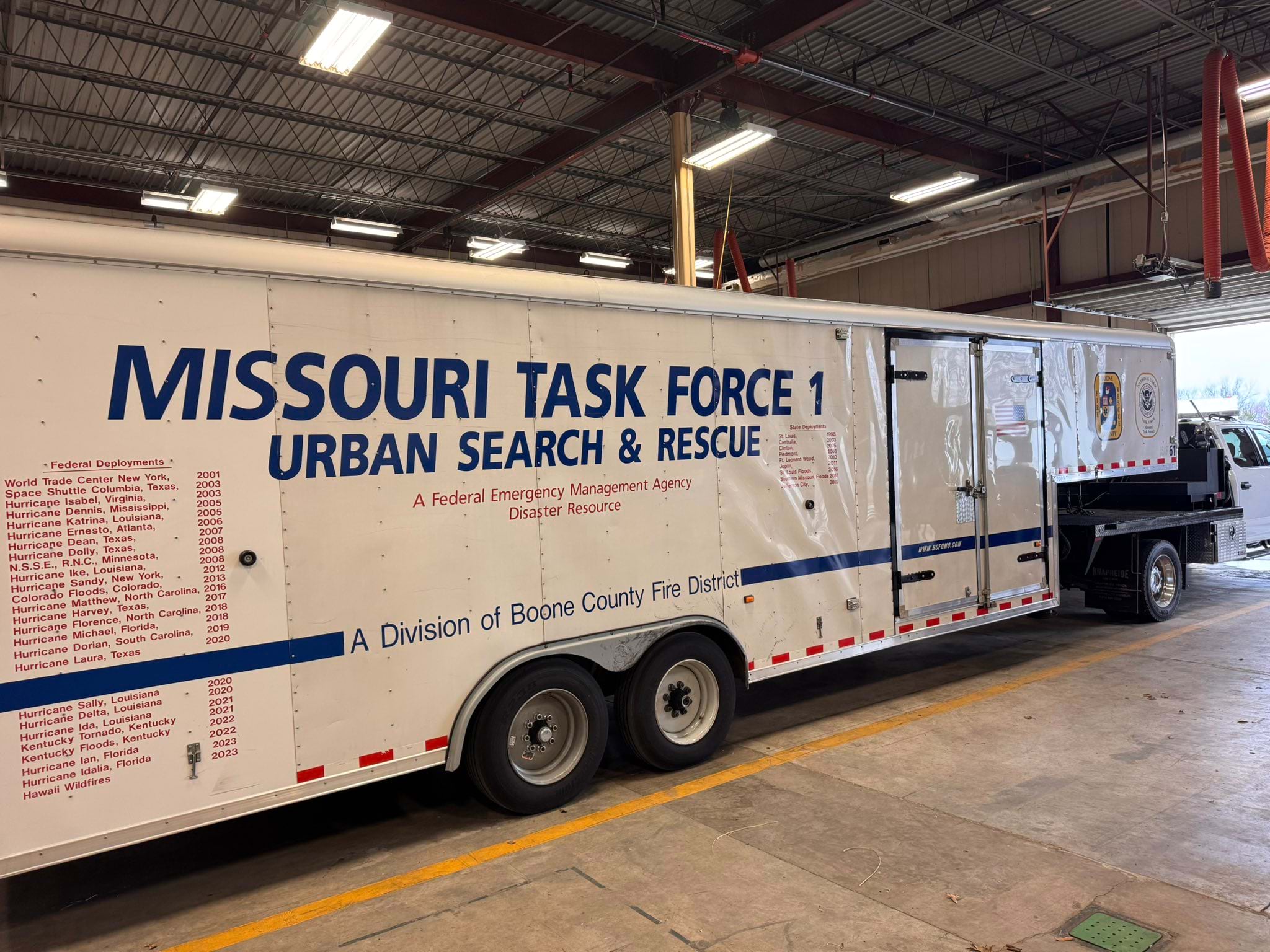 Large white trailer marked "Missouri Task Force 1 Urban Search & Rescue" with extensive list of federal deployments from 2001-2023 including World Trade Center, Space Shuttle Columbia, and numerous hurricane responses, parked in warehouse facility