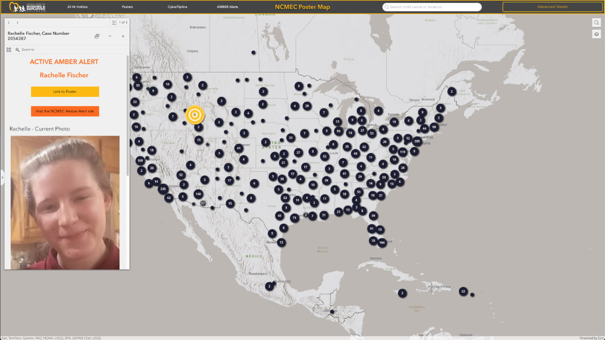 Screenshot of NCMEC's interactive map showing an active AMBER Alert popup for Rachelle Fischer (case number 2054387) with her photo and orange alert buttons. The map displays numbered dots across the United States representing missing children cases, with an orange circular target marker showing the user's location. The interface includes search functionality and an "Advanced Viewer" option.