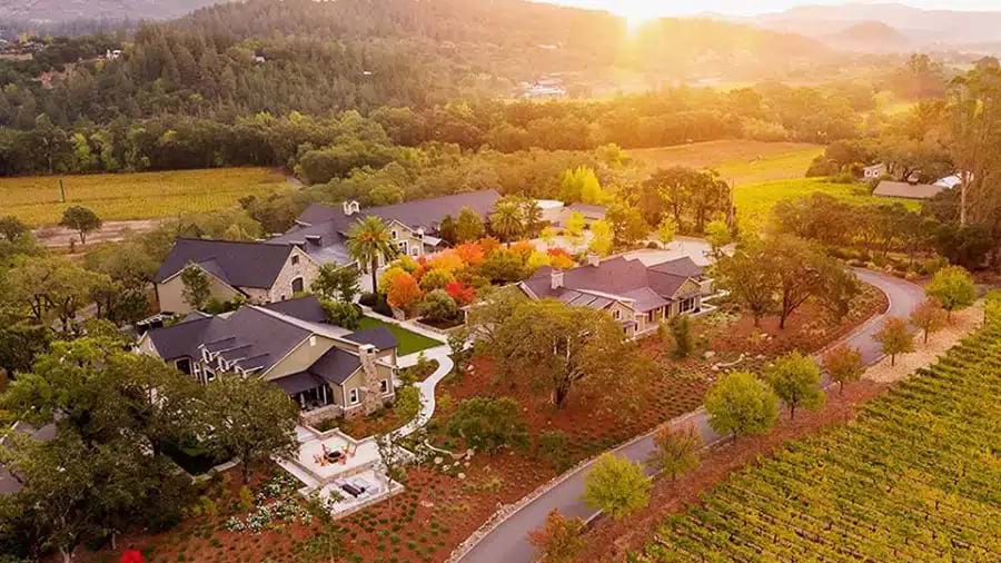 Aerial photograph of Trinchero winery estate at golden hour, showing main winery buildings surrounded by vineyards, with warm lighting highlighting the integration of facilities within the agricultural landscape.