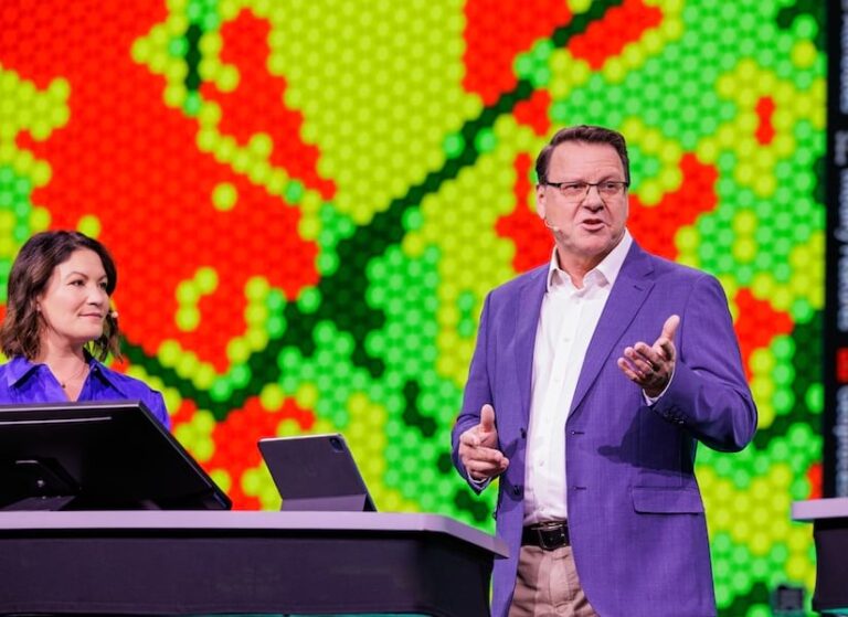 A man and woman presenting on a stage with a red and green geometric background behind them