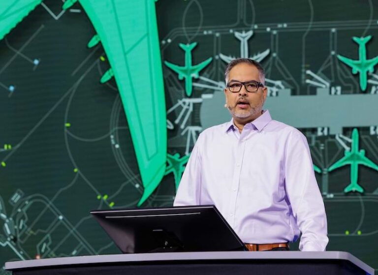 A professional man wearing glasses speaking at a podium