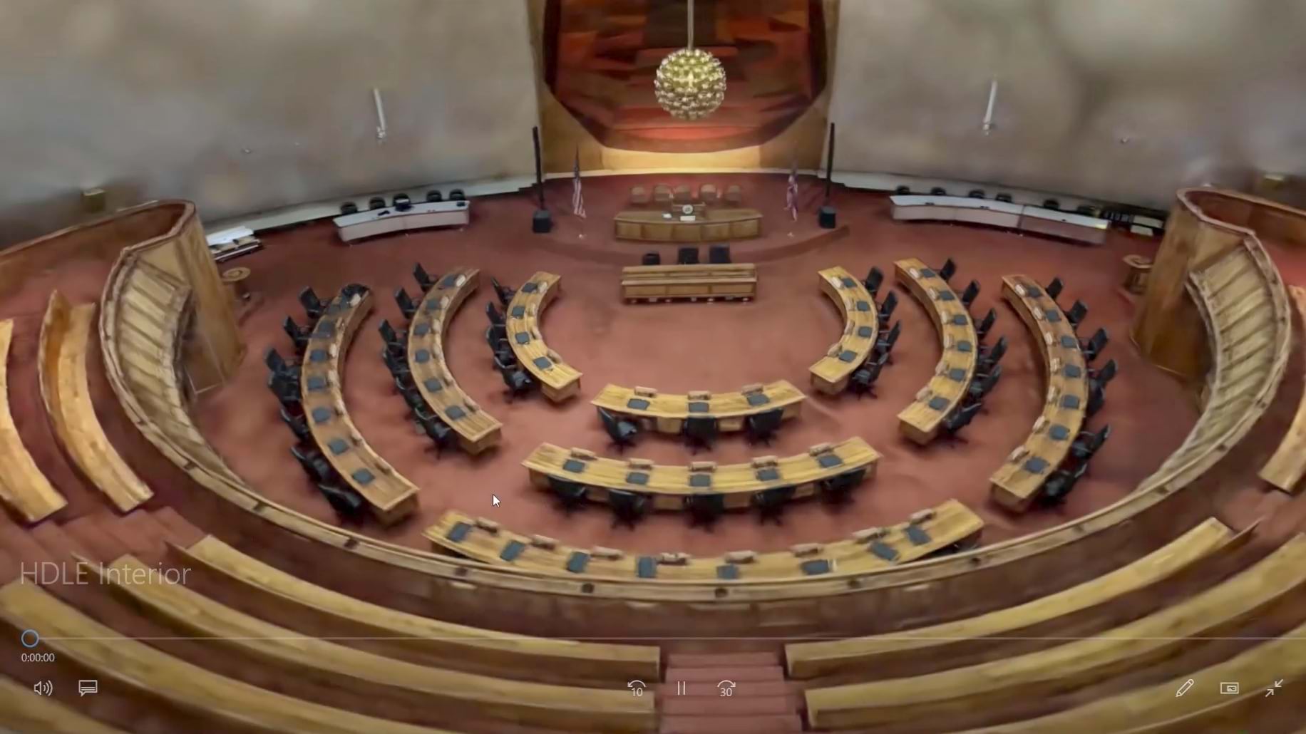 Interior view of Hawaii state capitol legislative chamber showing curved rows of wooden desks arranged in concentric semicircles around a central podium. The detailed 3D model displays the distinctive dome ceiling with decorative lighting and tiered gallery seating areas.
