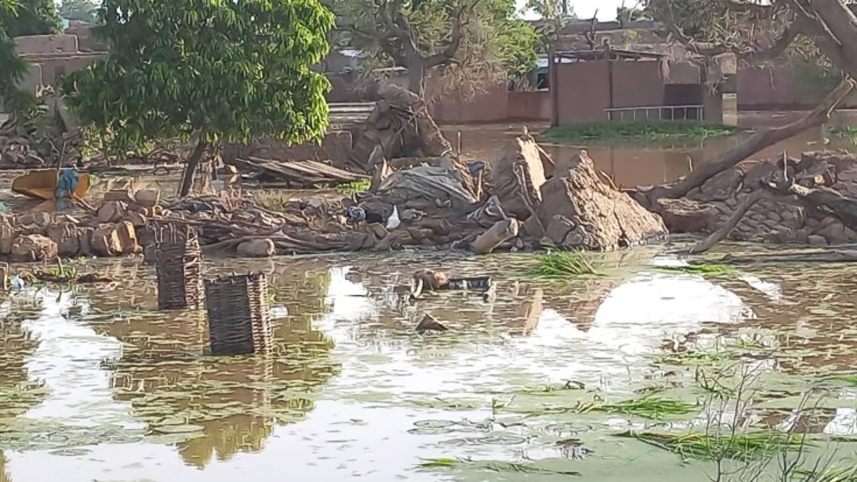Flood-damaged village in Mali with collapsed mud-brick buildings partially submerged in standing water, showing the aftermath of severe flooding that displaced thousands and destroyed homes and infrastructure.