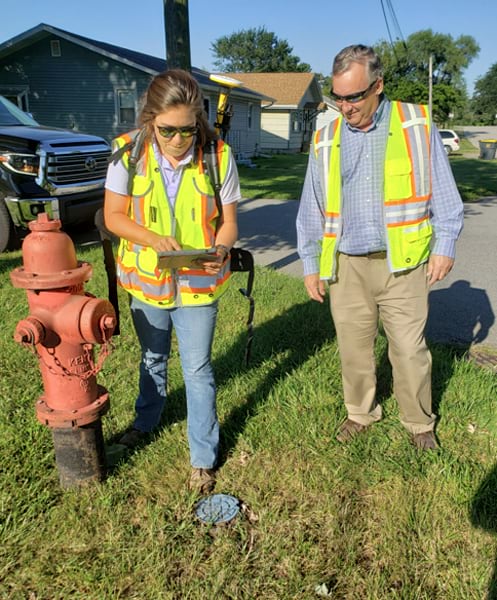 Photo of a man and a woman in high-visibility vests inspecting a fire hydrant. The woman is holding a tablet.