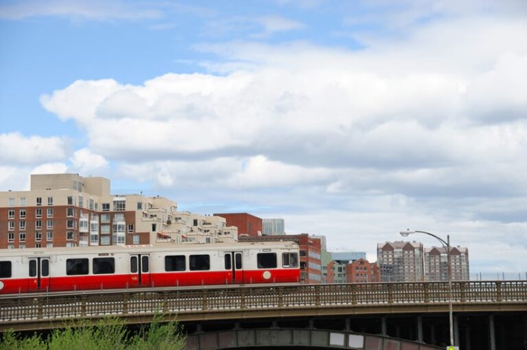 A photo of a red and white train with various multifamily buildings in the background.