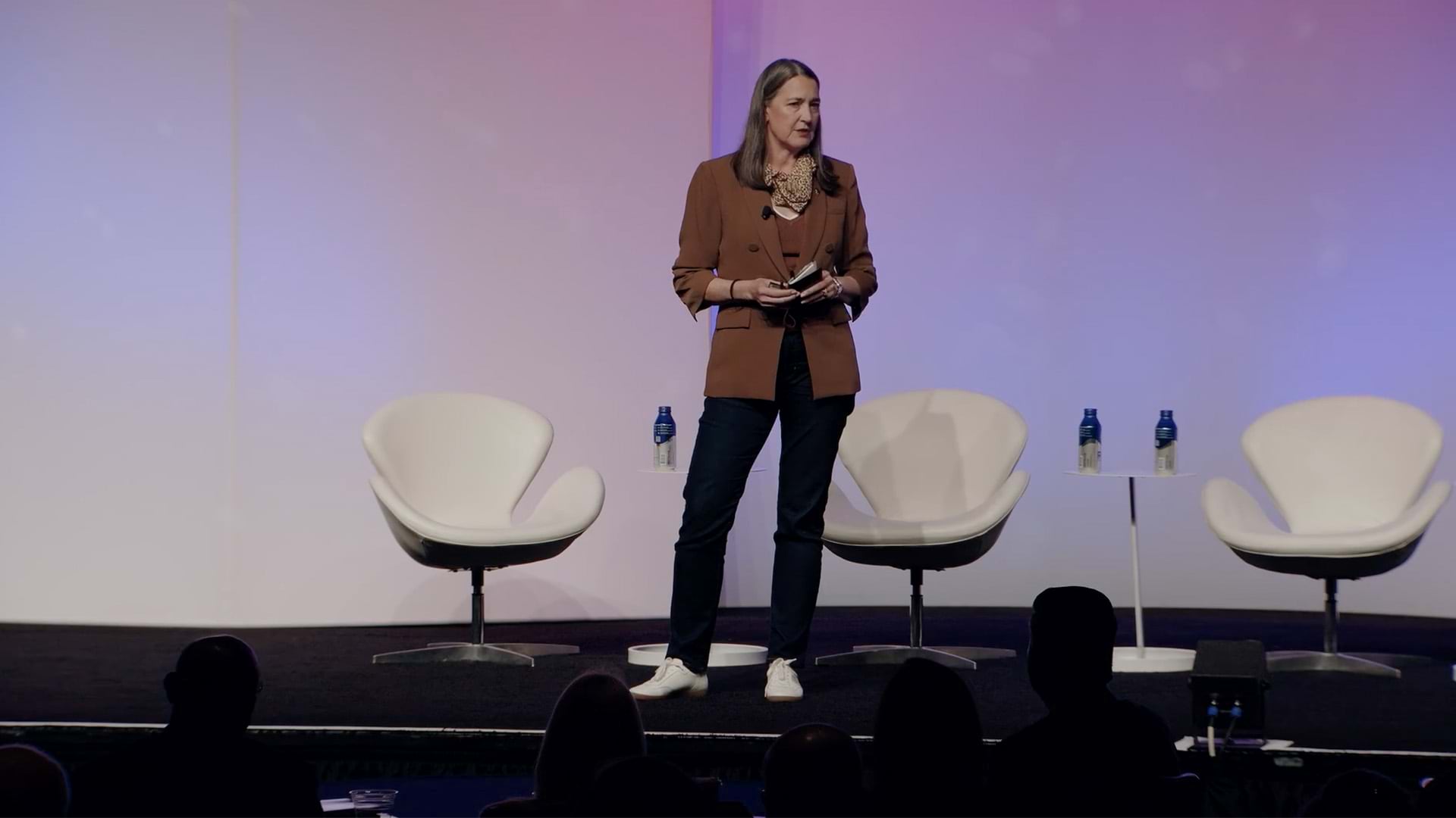 A person wearing business casual attire standing on a presentation stage backlit with a light purple gradient