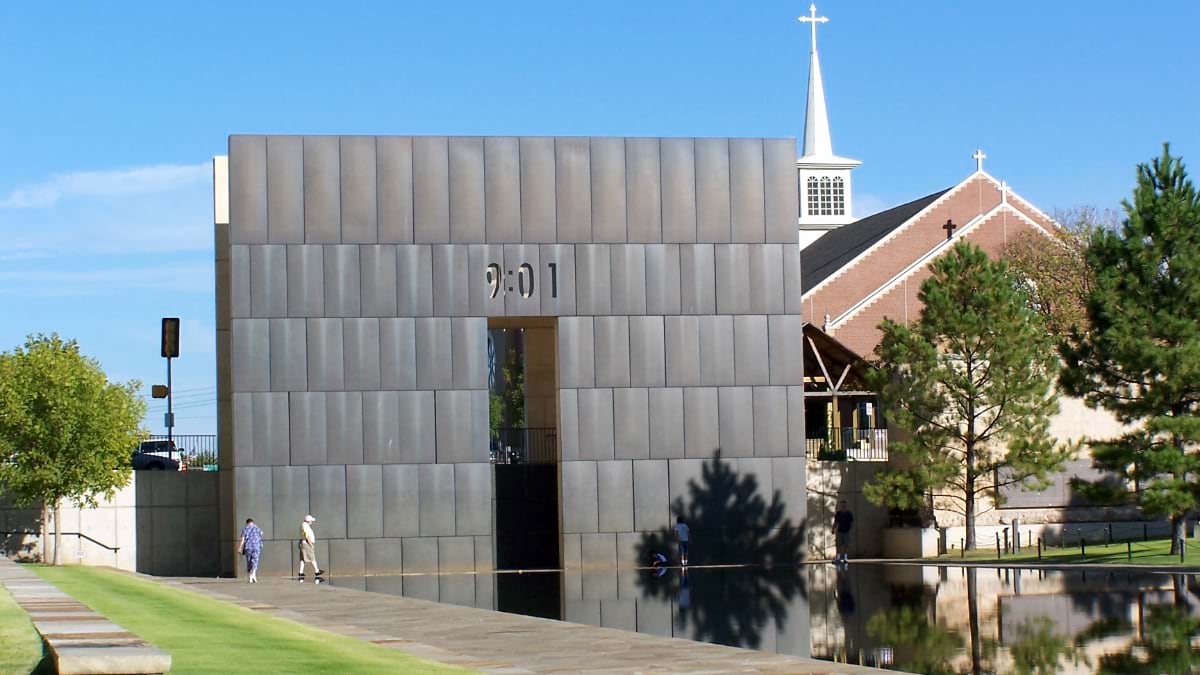 Oklahoma City National Memorial Gates of Time structure showing "9:01" with reflecting pool and church in background under blue sky.