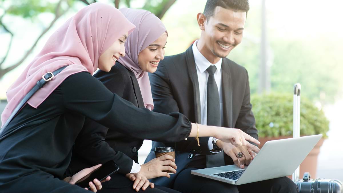 Three Malaysian health professionals viewing data on laptop together outdoors