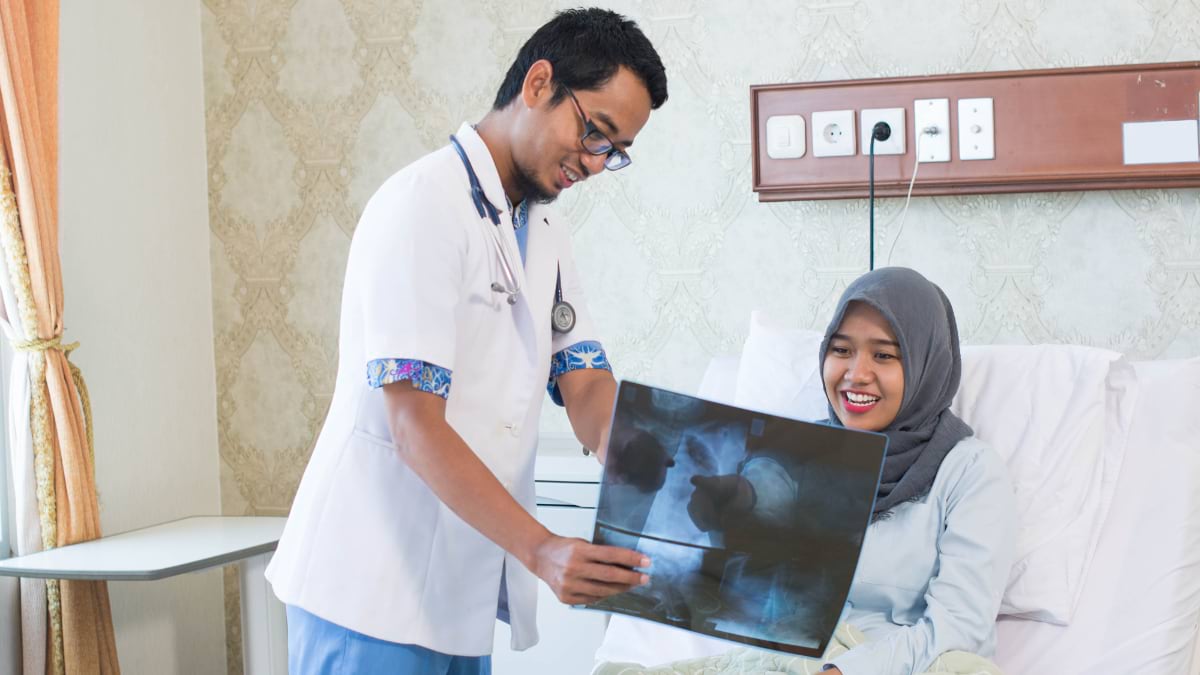 Doctor reviewing X-ray with smiling patient in Malaysian hospital room