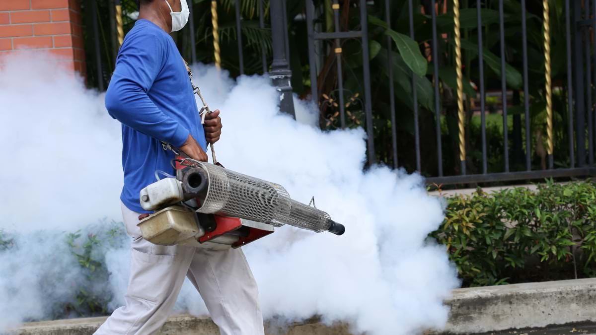 Health worker with fogging equipment treating area for disease-carrying mosquitoes in tropical community setting